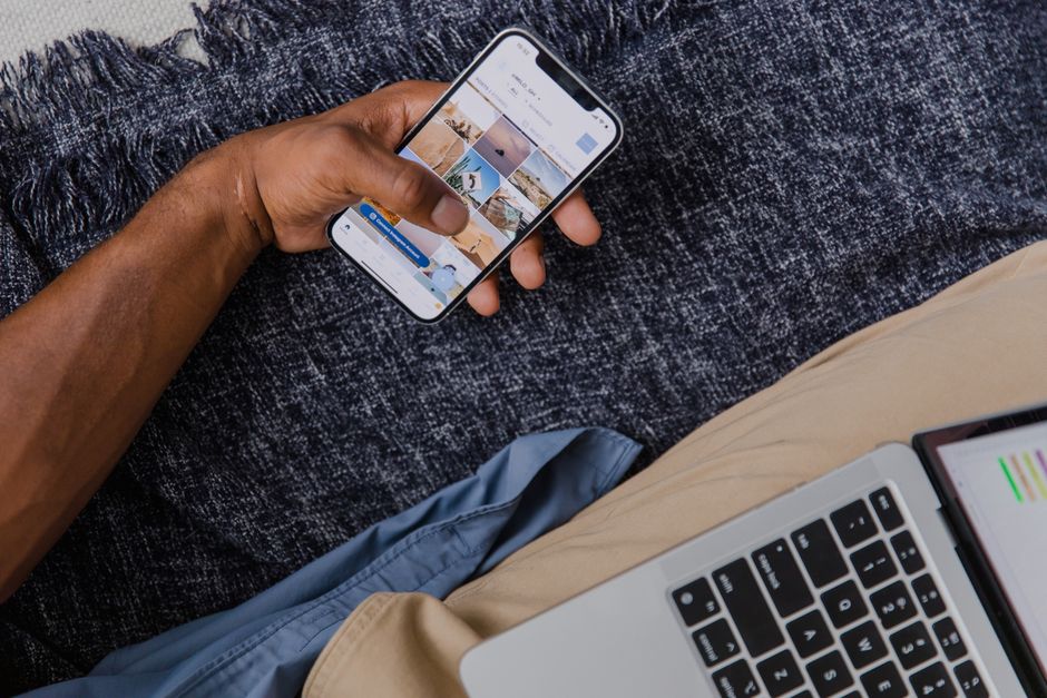 Main tenant un smartphone avec un ordinateur portable ouvert, illustrant le mode de vie numérique moderne.
