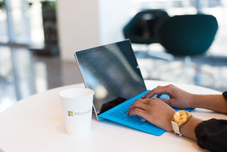 Mains tapant sur un clavier bleu avec une tasse marquée d'une marque sur une table.