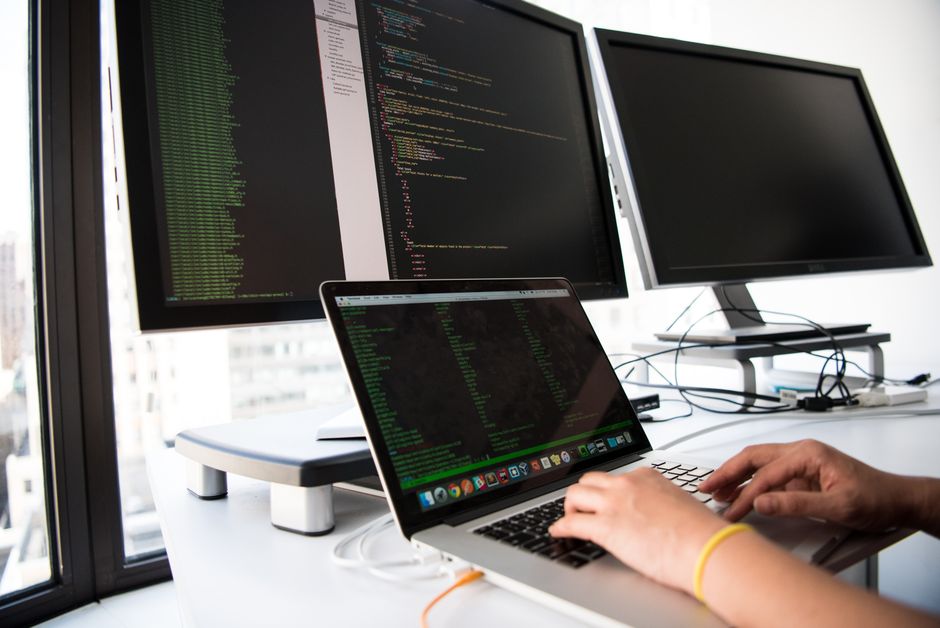 Développeur écrivant du code sur un ordinateur portable devant plusieurs écrans dans un environnement de bureau.