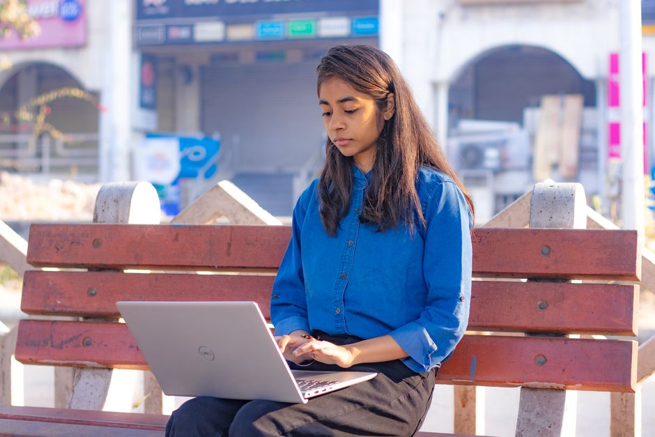 Jeune femme assise sur un banc en extérieur, concentrée sur son ordinateur portable en ville, en journée.