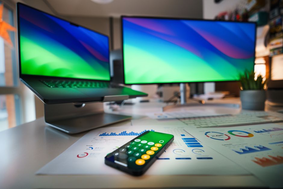 Bureau contemporain avec un ordinateur portable, une application de calculatrice sur smartphone et des graphiques commerciaux.