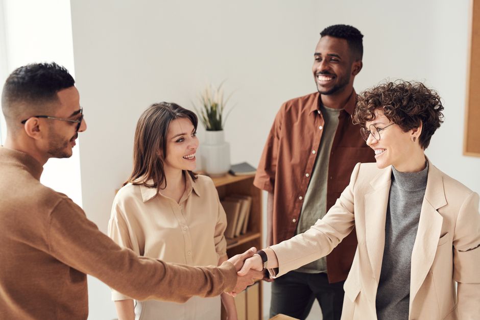 Quatre collègues souriants se serrant la main dans un bureau lumineux.