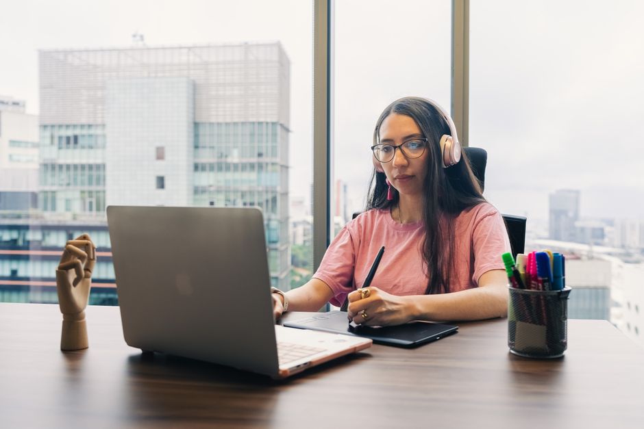 Femme professionnelle utilisant un ordinateur portable et un stylet dans un bureau moderne, portant un casque.