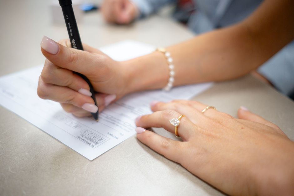 Vue détaillée de mains remplissant un formulaire, ornées de bijoux élégants et d'une manucure soignée.