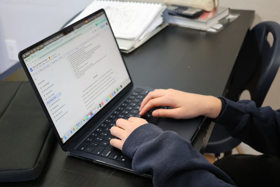 Personne tapant sur un ordinateur portable à un bureau avec des papiers et des livres à proximité.