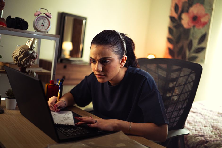 Jeune femme étudiant intensément sur un ordinateur portable à un bureau bien éclairé en intérieur.