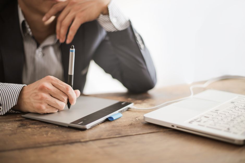 Homme élégant regardant son ordinateur portable tout en dessinant sur une tablette graphique à un bureau en bois.