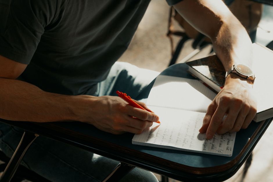 Un étudiant concentré prend des notes dans un carnet pendant un cours.