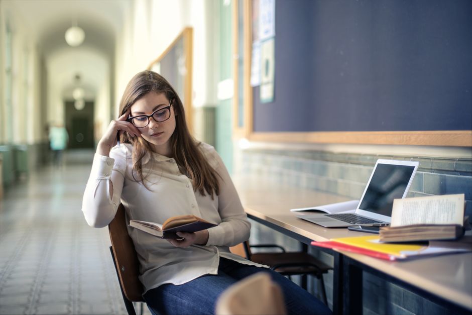 Une jeune femme étudie avec diligence dans un couloir d'université en lisant un livre.