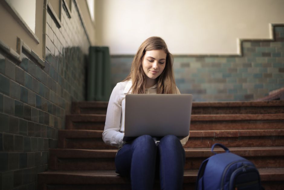 Une jeune femme assise dans des escaliers utilisant un ordinateur portable pour le télétravail, idéal pour promouvoir le style de vie de nomade numérique.