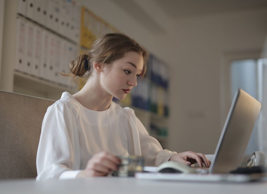 Femme concentrée en blanc travaillant sur un ordinateur portable dans un bureau moderne.
