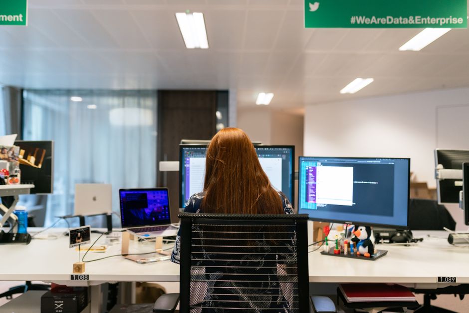 Vue de dos d'une ingénieure en logiciel travaillant sur une configuration multi-écrans dans un bureau.