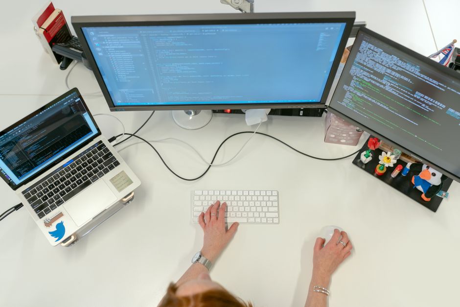 Ingénieure logicielle travaillant sur deux écrans et un ordinateur portable dans un bureau.