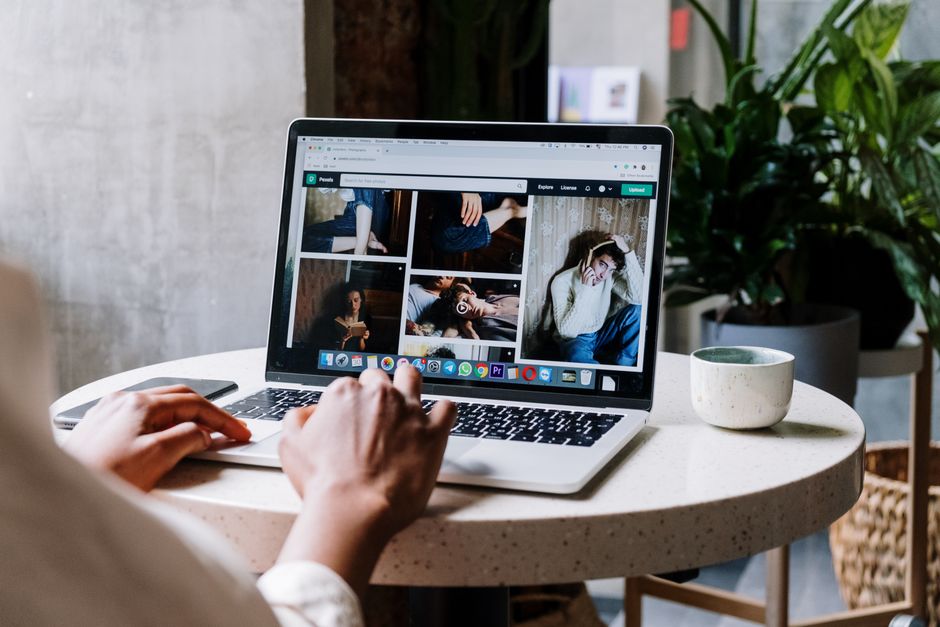 Personne consultant des photos sur un ordinateur portable à une table ronde, accompagnée d'un mug et de plantes en intérieur.