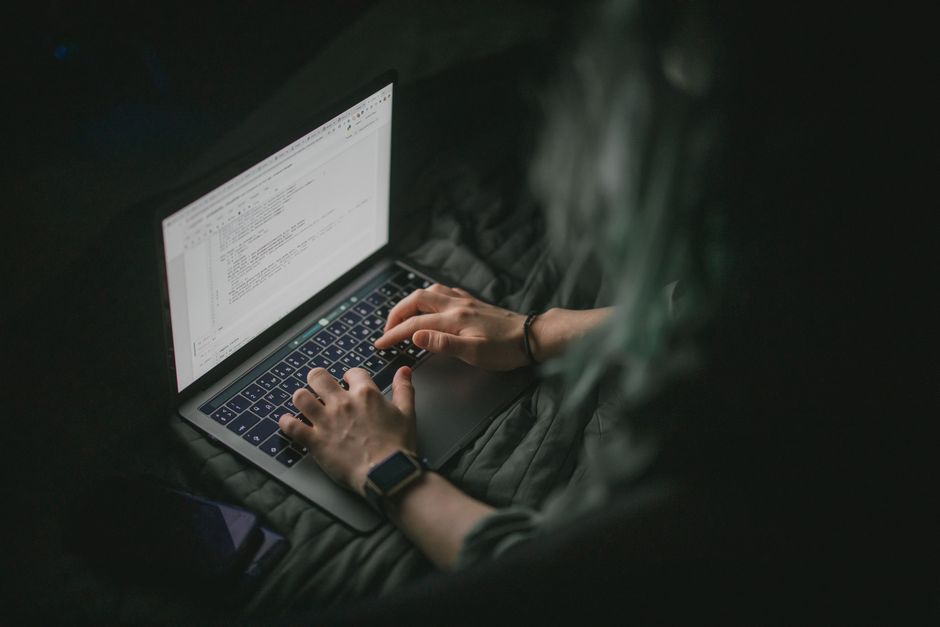 Gros plan sur des mains tapant sur un ordinateur portable avec du code à l'écran, parfait pour le travail à domicile et les thèmes technologiques.