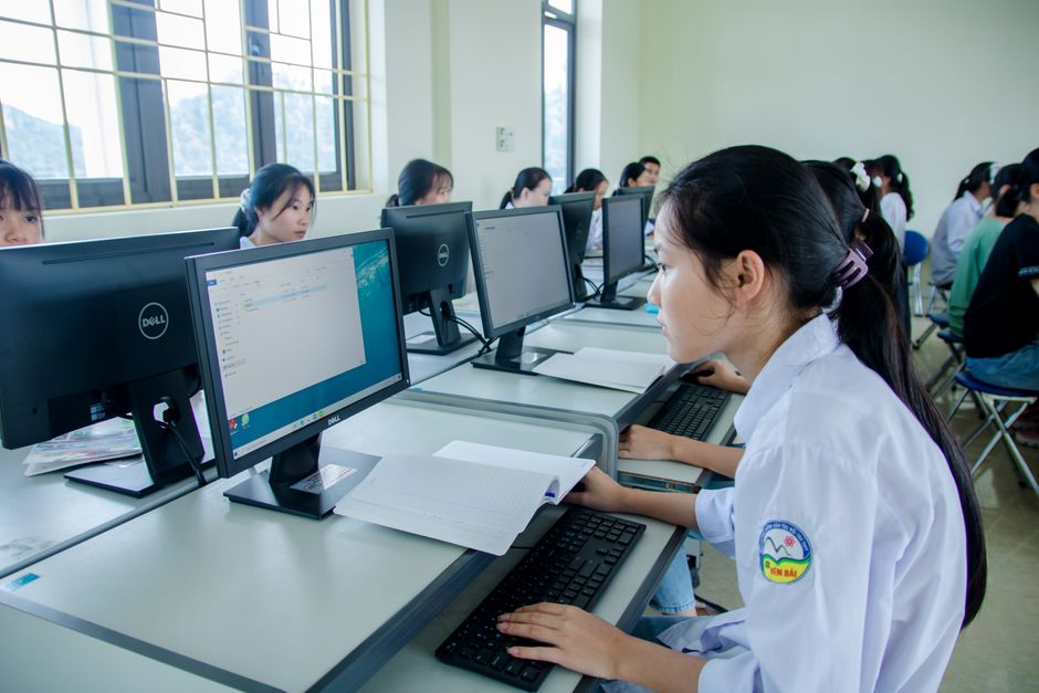 Groupe d'étudiants asiatiques travaillant ensemble dans une salle informatique, axé sur le travail d'équipe et la technologie.