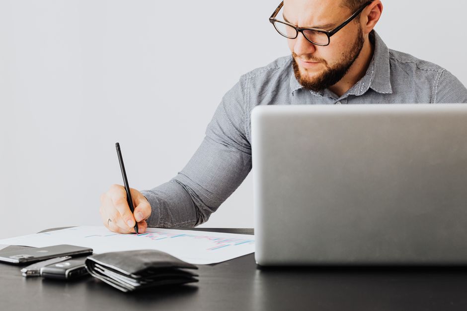 Homme concentré analysant des documents financiers sur un ordinateur portable dans un bureau.