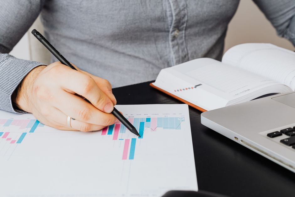 Analyste commercial étudiant un graphique sur papier, entouré d'un ordinateur portable et d'un carnet, en intérieur.