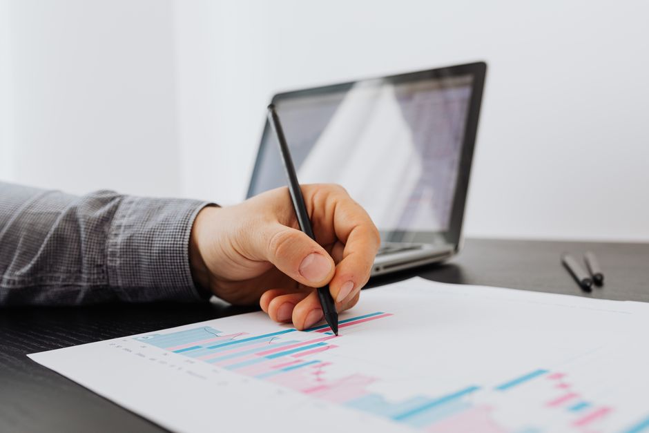 Personne prenant des notes sur un graphique professionnel avec un ordinateur portable en arrière-plan.