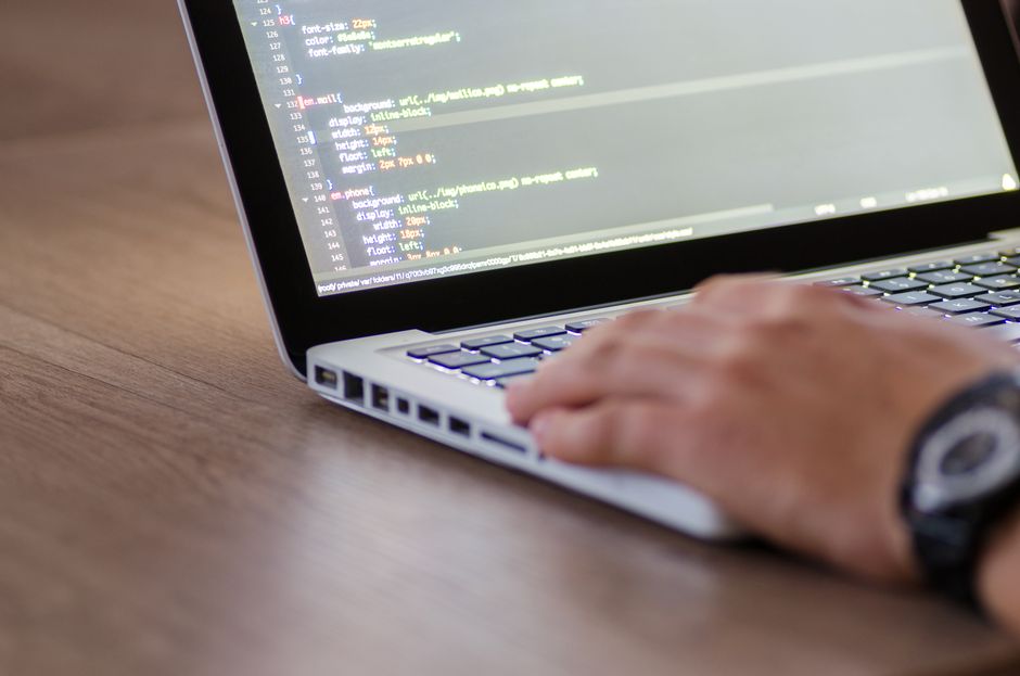 Personne programmant sur un ordinateur portable affichant du code HTML, illustrant un travail de développement.