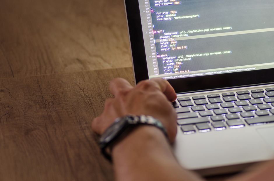 Main d'un développeur interagissant avec du code sur l'écran d'un ordinateur portable dans un espace de travail.