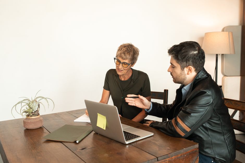 Femme âgée et homme adulte collaborant sur un ordinateur portable en intérieur.