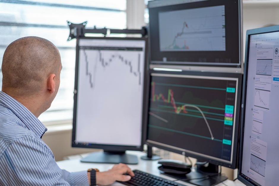 Trader analysant des données financières sur plusieurs écrans dans un environnement de bureau.
