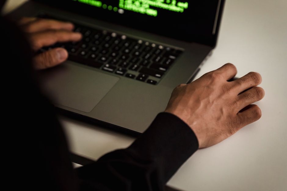 Vue en plongée d'un développeur sans visage en sweat à capuche noir écrivant du code sur un netbook dans un studio lumineux.