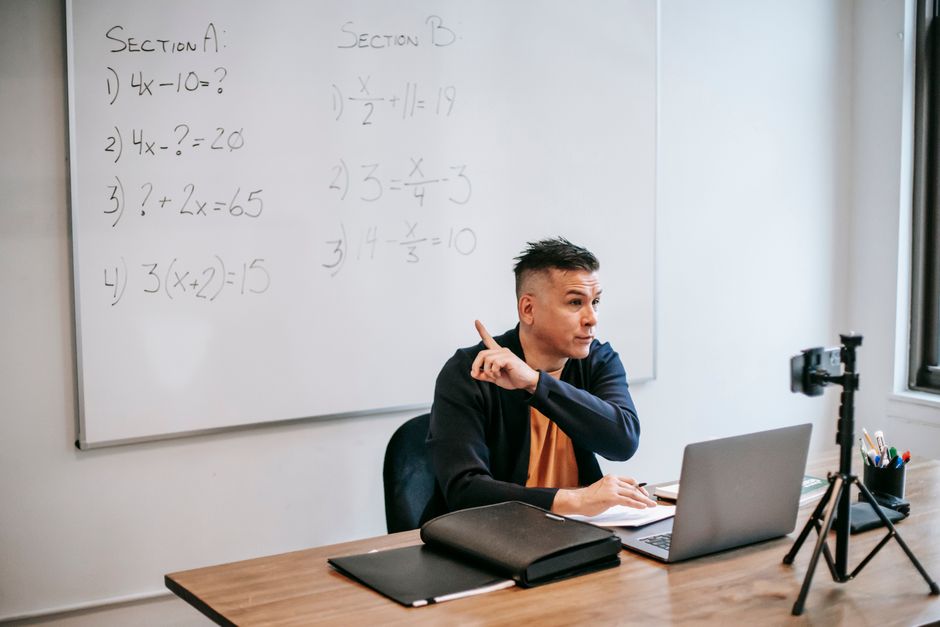 Enseignant expliquant des équations mathématiques lors d'un cours en ligne, utilisant un ordinateur portable et un tableau blanc.
