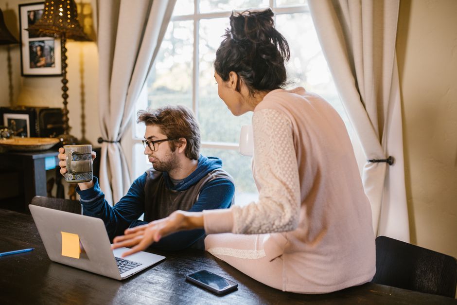 Couple engagé dans une discussion animée en intérieur avec un ordinateur portable ouvert sur la table.