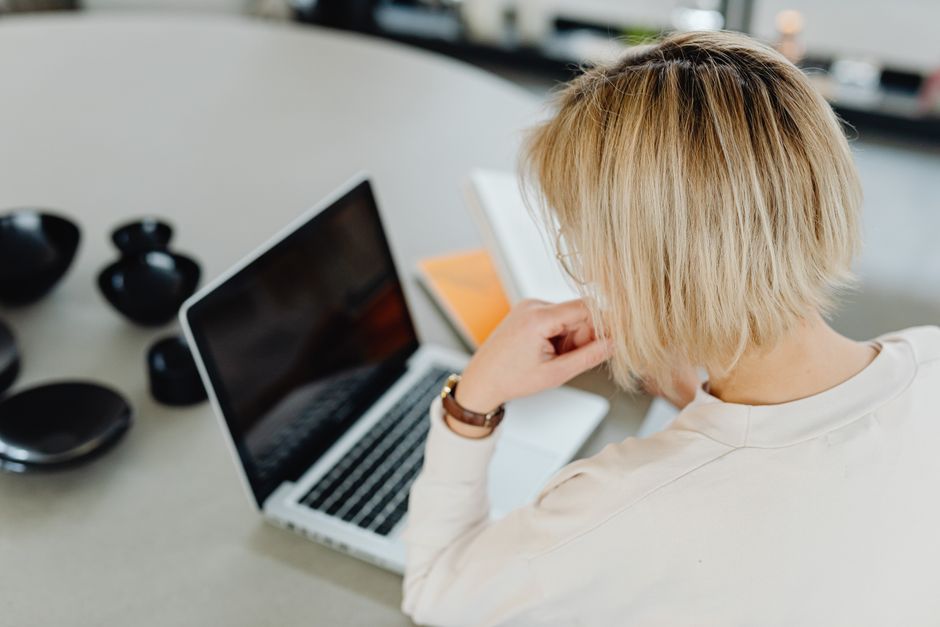 Une femme aux cheveux courts blonds travaillant sur un ordinateur portable à domicile.