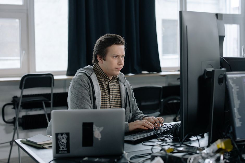 Programmeur concentré sur son travail de codage avec deux écrans dans un bureau moderne.