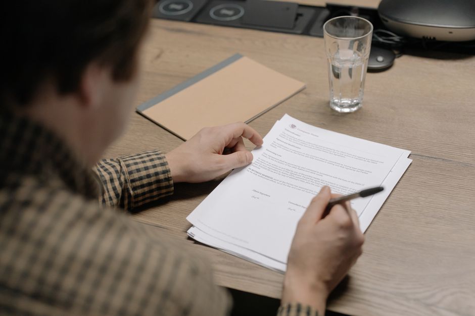Un homme d'affaires examine un contrat en tenant un stylo, avec un verre d'eau posé sur le bureau à proximité.