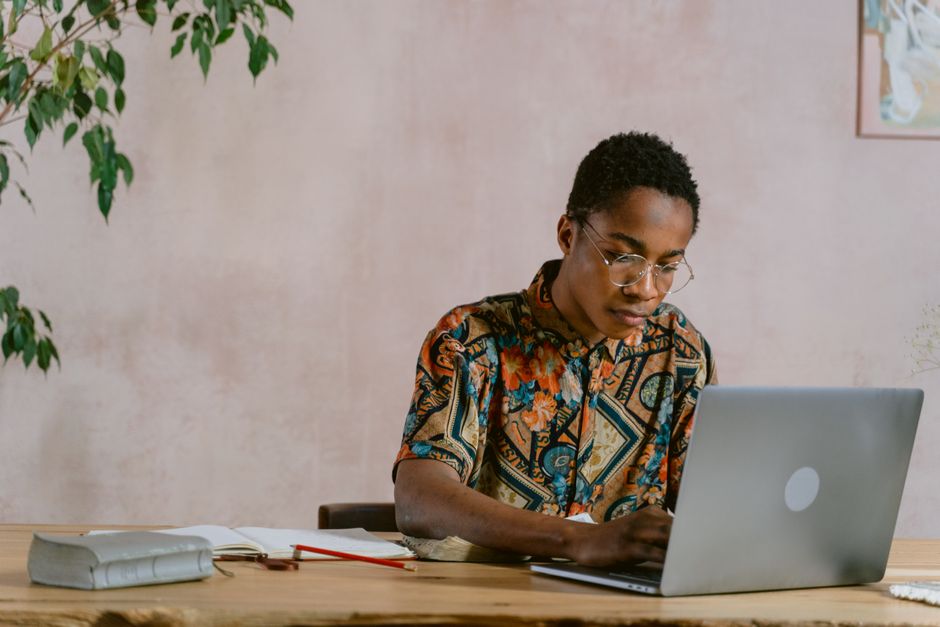 Jeune homme à lunettes travaillant sur un ordinateur portable à une table en bois dans un intérieur chaleureux.