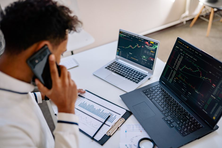 Homme analysant des graphiques boursiers sur des ordinateurs portables tout en parlant au téléphone.