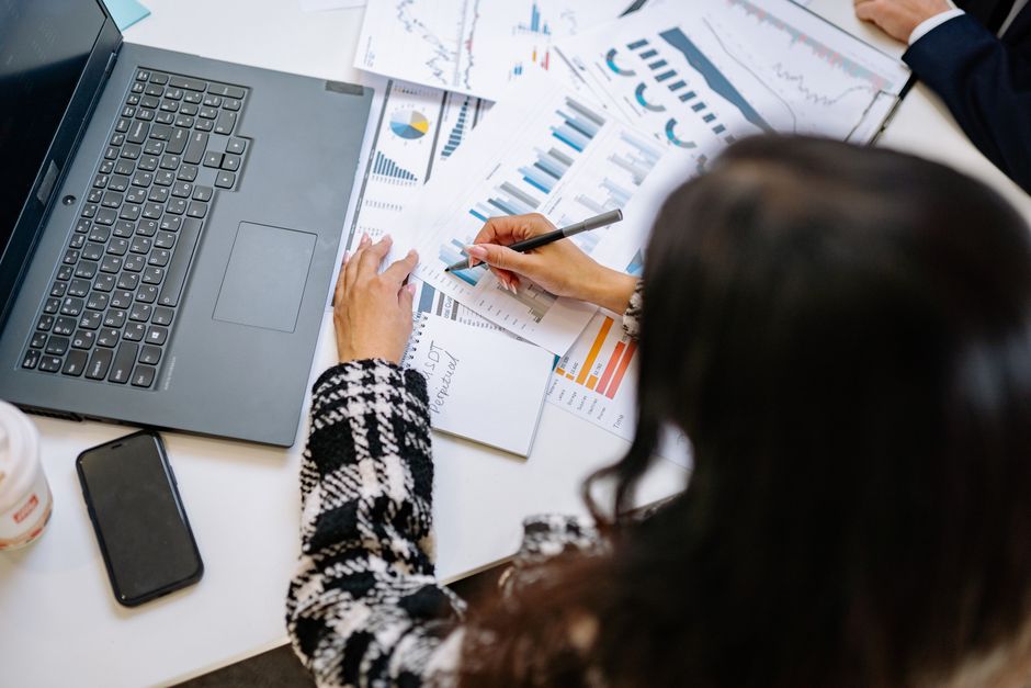 Une professionnelle examine des tableaux et graphiques financiers avec un ordinateur portable et un smartphone sur son bureau.