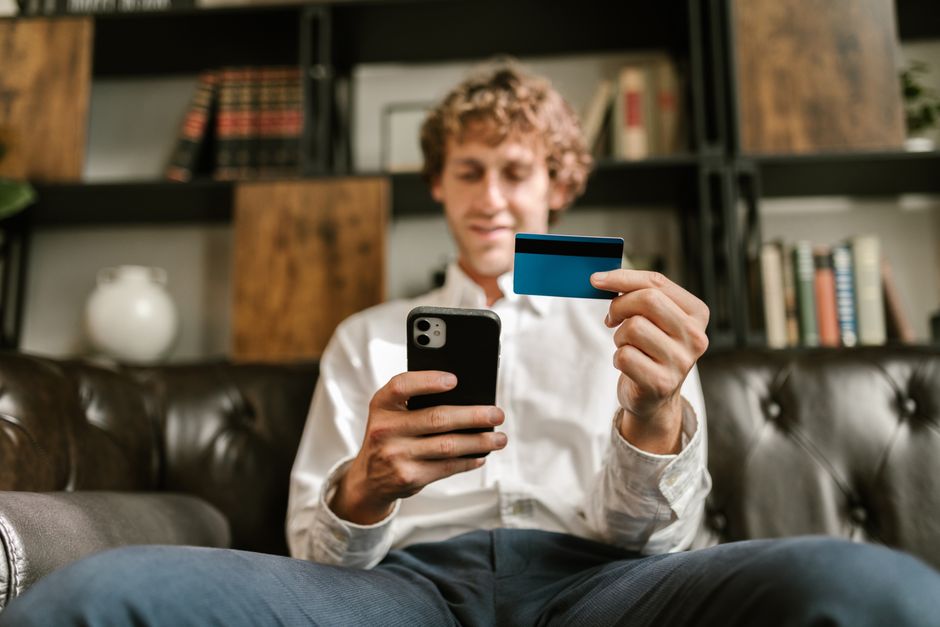 Homme souriant utilisant son smartphone et une carte de crédit pour faire des achats en ligne.