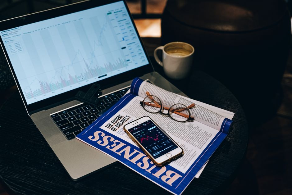 Espace de travail professionnel avec un ordinateur portable, un smartphone, une tasse de café et un magazine économique sur une table.