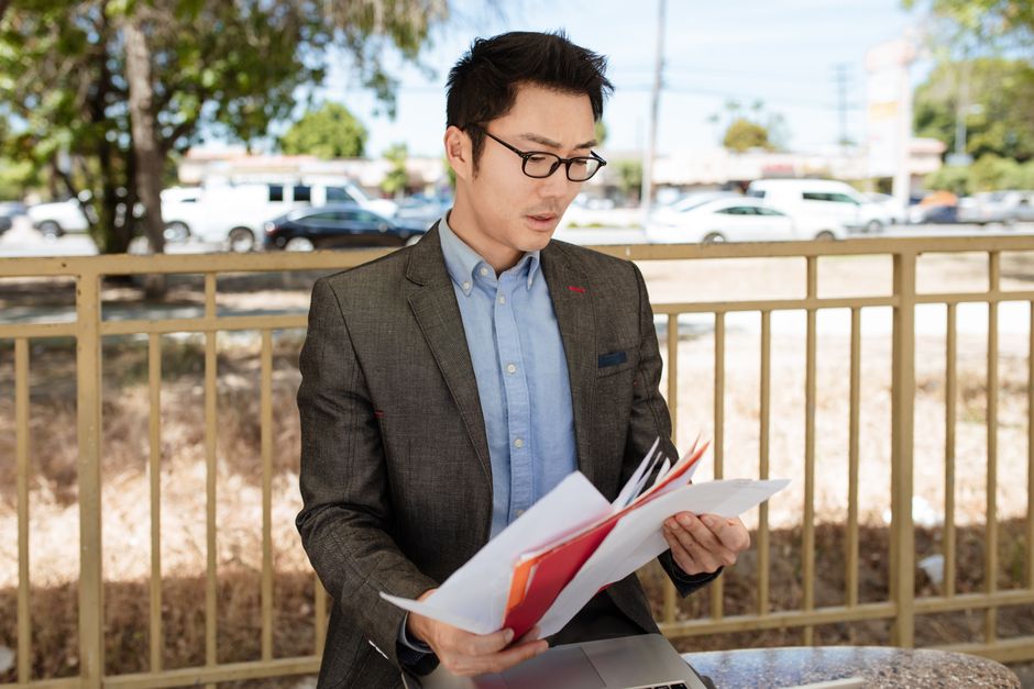 Homme d'affaires asiatique en costume consultant des documents en extérieur par une journée ensoleillée.