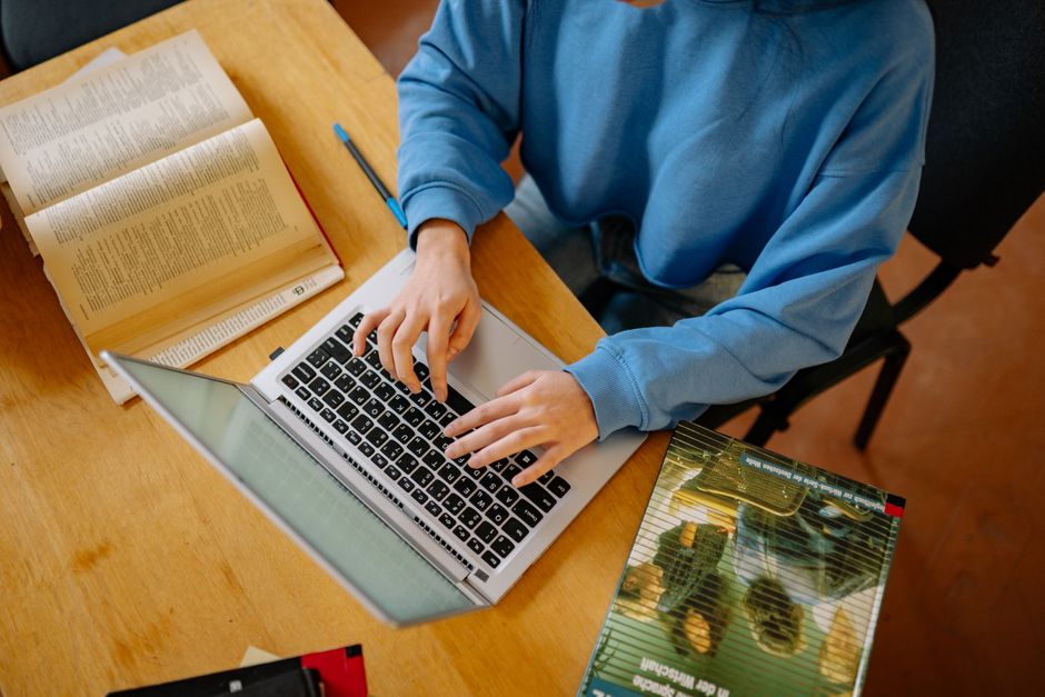 Étudiant tapant sur un ordinateur portable au milieu de livres ouverts, concentré sur ses recherches et son travail scolaire.