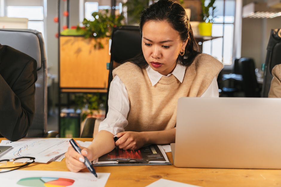 Femme au bureau travaillant sur des graphiques et un ordinateur portable, concentrée sur l'analyse de données.
