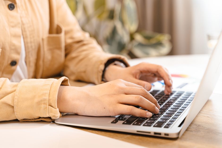Gros plan sur des mains tapant sur un ordinateur portable dans un intérieur lumineux, illustrant le travail et la technologie.