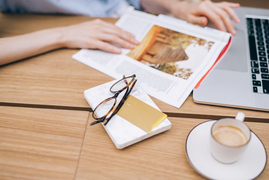 Un espace de travail chaleureux avec un ordinateur portable, une tasse de café, un magazine et des lunettes sur une table en bois.